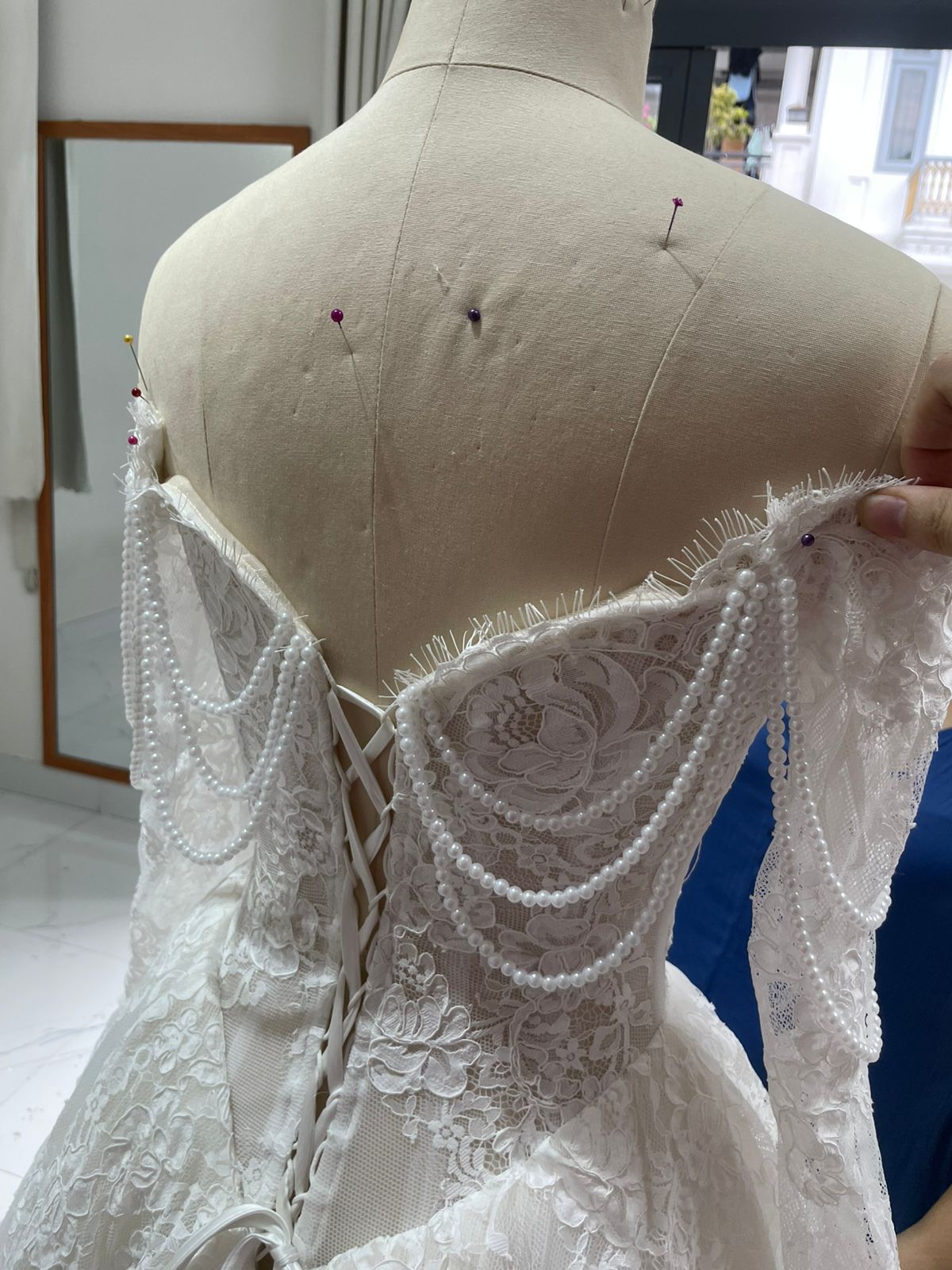 Final QC back detail showing corset lacing, lace sleeves, and string pearl draping on Bianca's custom wedding dress