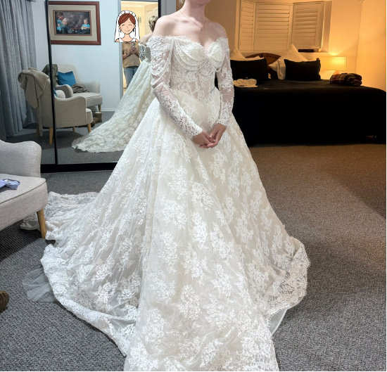 Client try-on front view of Bianca's premium lace A-line wedding dress showing off-shoulder sleeves, pearl draping, and full skirt