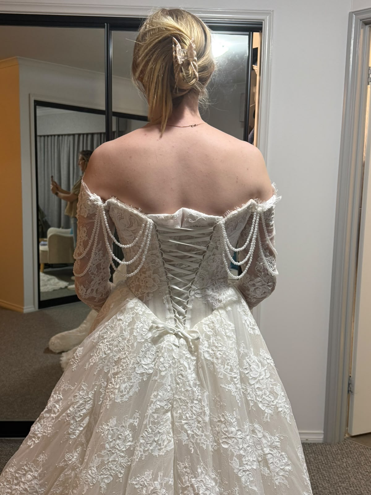 Client try-on back view of Bianca's premium lace A-line wedding dress showing corset lacing and string pearl draping